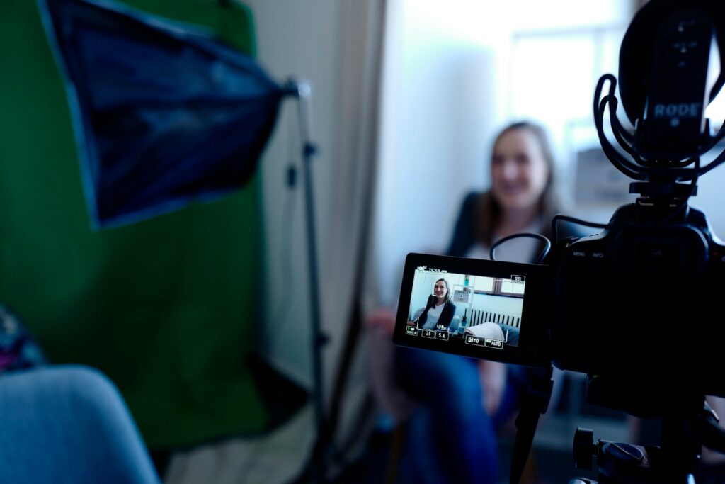 Homepage Woman being recorded in a professional studio setup, using video camera and lighting equipment.