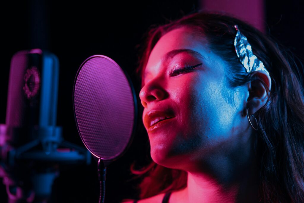 Homepage Close-up of a woman passionately singing into a studio microphone with vibrant lighting.